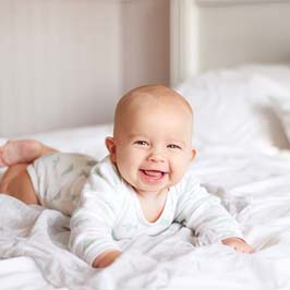 A happy baby lying on its stomach on a bed