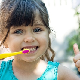 Girl with toothbrush giving thumbs up for fighting cavities