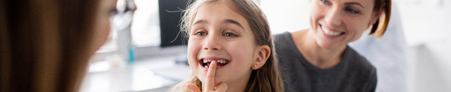 excited child shows the dentist her teeth with her mother beside her