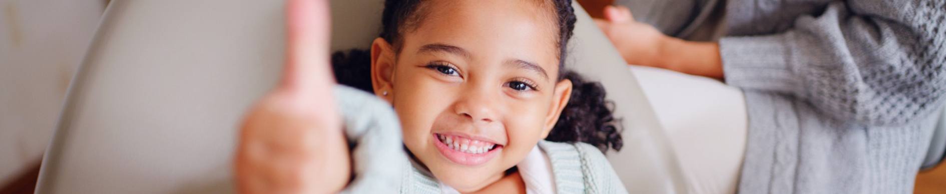smiling little girl holding a thumbs up in the dental chair