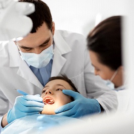 A dentist examining a young boy’s smile before beginning the process of placing a dental crown