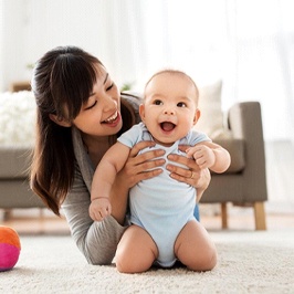 A mother on the floor with her baby who is smiling and playing with a ball