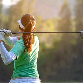 A female wearing a polo shirt and visor swinging a golf club during a game