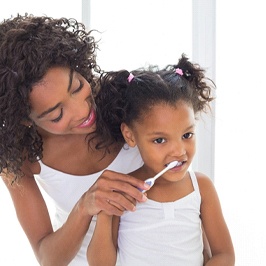 A mother helping her young daughter brush her teeth