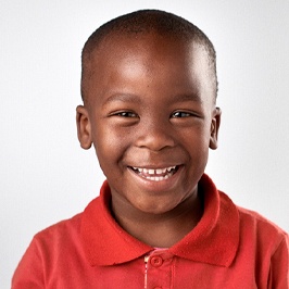 A young boy wearing a red polo shirt and showing off his happy, healthy smile