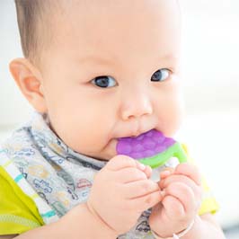 A baby wearing a bib and chewing on a teething toy to relieve discomfort caused by teething