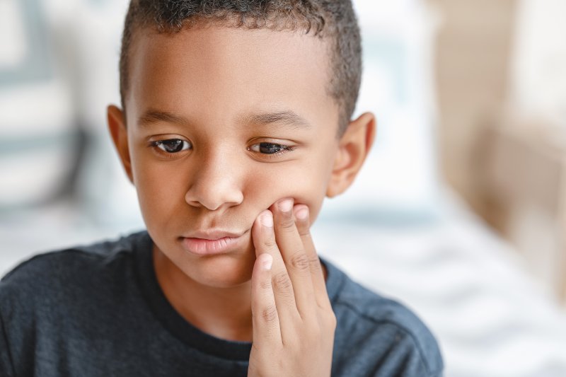 a young boy holding his cheek because of pain caused by a toothache