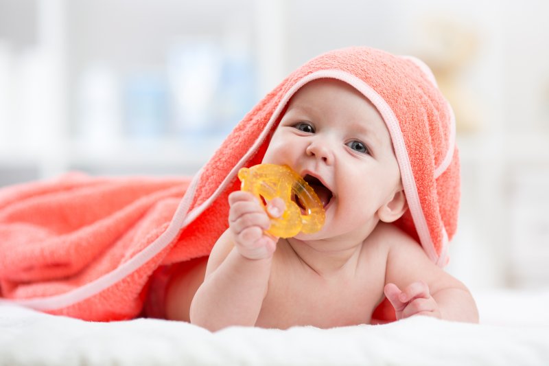 a baby wearing a towel and lying on a bed while chewing on a teether