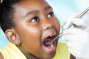 a little girl opening her mouth wide so her dentist can examine her oral cavity