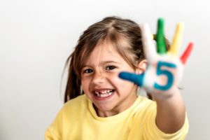 girl smiling holding up her hand for 5 facts about children’s dental health