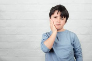 little boy holding his face with a dental emergency