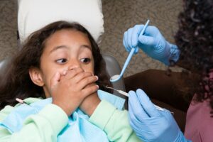 little girl covering her mouth when pediatric dentist tries to look