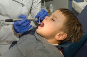little boys with his mouth open for dental work and eye closed