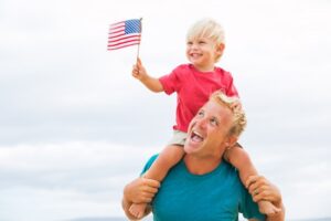 father holding a son on his shoulders with an American flag
